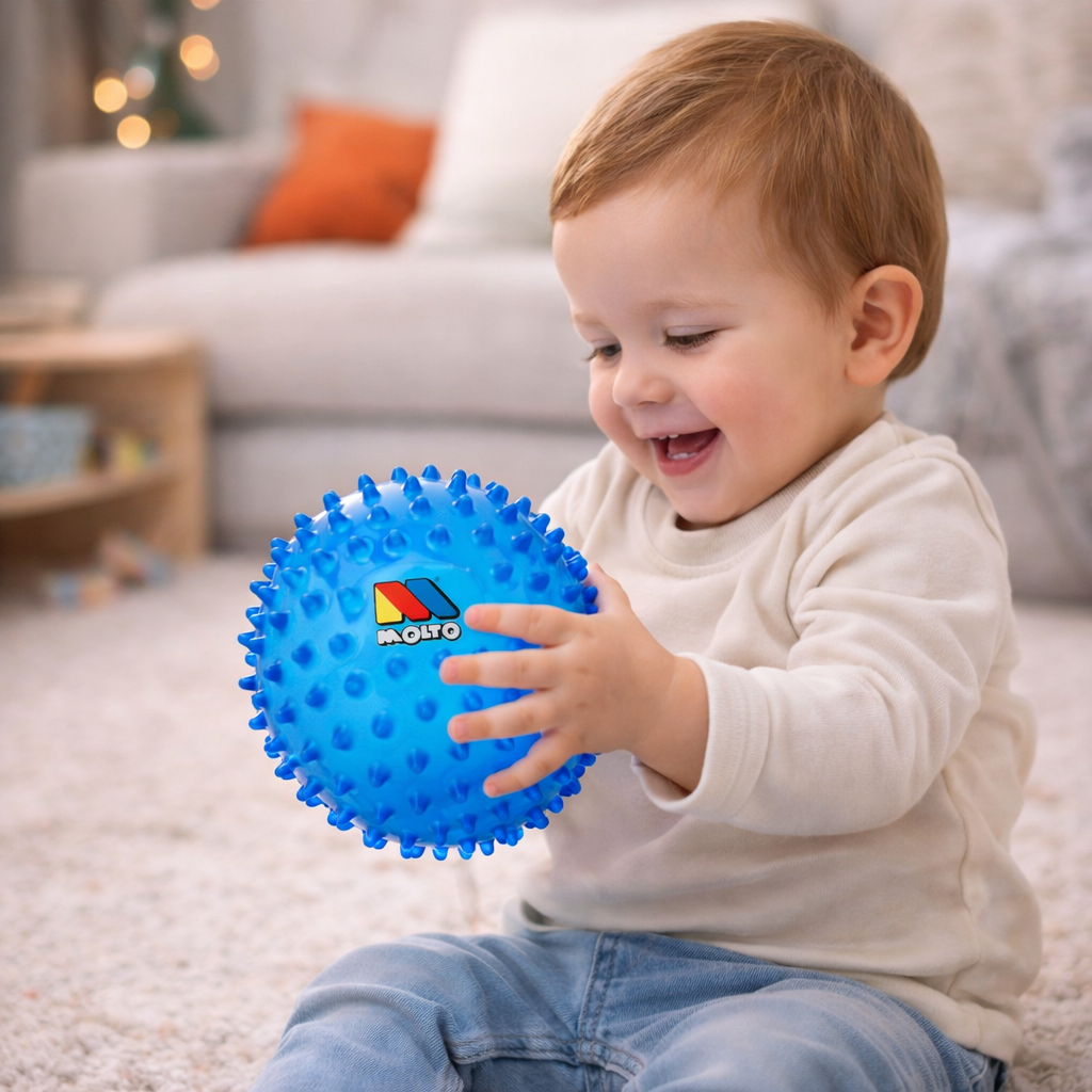 Bébé souriant jouant avec une balle sensorielle Moltó bleue pour développer la coordination et la motricité.